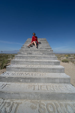 March 23, 2019 - North Shore, California: Young woman sits on top of a staircase in the middle of the desert, that overlooks the Salton Seaの写真素材