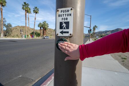 Rancho Mirage, California - March 22, 2019: Caucasian female hand pushes the button for the pedestrian walk signal to cross in a crosswalkの写真素材