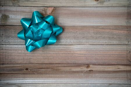 One single teal blue gift package bow on a brown wood background. Useful for birthday party or Christmas concepts and flat layの写真素材