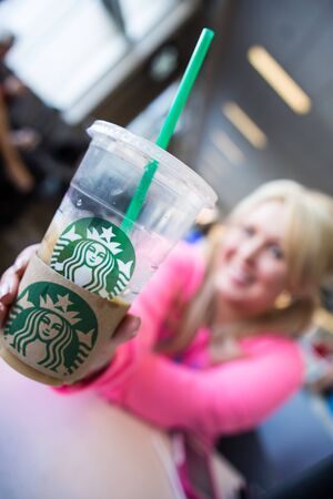 Minneapolis, MN - May 2 2018: Blonde female holds up a Starbucks coffee drink at an airport. Intentionally blurred woman to focus on the beverageのeditorial素材