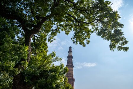 Qutub Minar minaret pillar framed by trees against a blue sky in New Delhi Indiaの写真素材