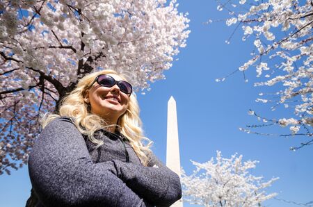Blonde woman poses with a sense of achievement and accomplishment near the Washington Monument with Cherry Blossom trees in full bloomの写真素材