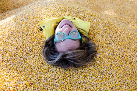 An adult female has her entire body covered and buried in corn kernels in a corn pit, with only her head showingの写真素材
