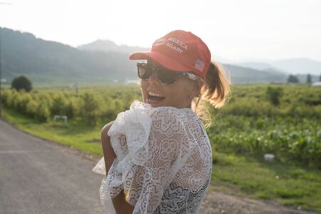 Wenatchee, Washington - July 4, 2019: Cute Republican woman wearing a MAGA hat (Make America Great Again) supporting President Donald Trump and his 2020 re-election campaign, smiles wearing sunglassesのeditorial素材
