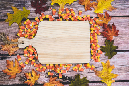 Halloween autumn and fall concept. Blank wooden cutting board for text, with candy corn and leaves...