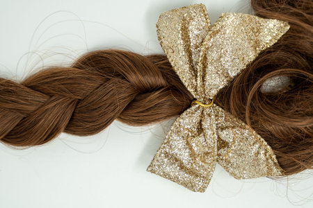 Beautiful braided brown hair isolated on white, glittery gold bow attached at the end of the braid.