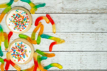 Iced sugar cookies with rainbow sprinkles and gummy worms. Wooden background with copy space...