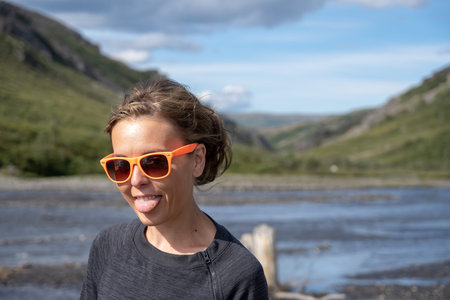 Adult female woman wearing orange beach sunglasses smiles and sticks tongue out. Photo taken at...