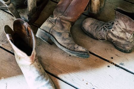Old abandoned vintage cowboy boots sit on a dusty wooden plank floor.の写真素材