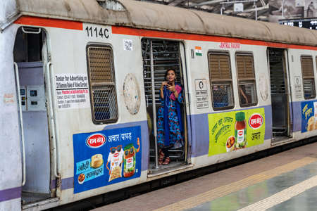Mumbai, India - February 29, 2020: Young Indian woman stands in the train railcar doorway with a phone at Chatrapati Shivaji Terminus earlier known as Victoria Terminusのeditorial素材