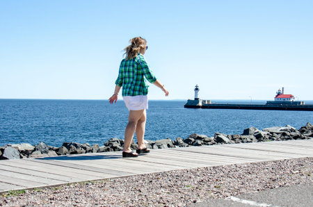 Adult female takes a relaxing stroll on Duluth Canal Park Lakewalk along Lake Superior. Lighthouses...