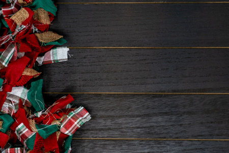 Festive Christmas red, green and white rag fabric garland over black wood background. Copy space...