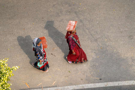 New Delhi, India - March 21, 2020: Two Indian woman walk with empty balancing boards for carrying construction materials on top of head, working at a construction siteのeditorial素材