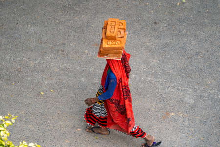 New Delhi, India - March 21, 2020: Indian woman wearing a sari walks while carrying and balancing bricks on her head, working at a construction siteのeditorial素材