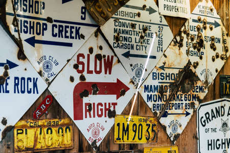 JULY 9 2018 - BISHOP, CALIFORNIA: Old antique vintage California road signs from the Eastern Sierra on display on a wall. Most signs are shot up with bullet holesのeditorial素材