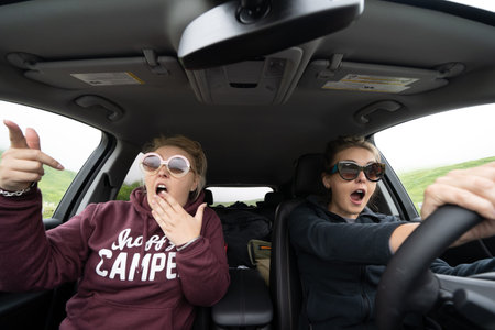 Two woman inside of a car looked shocked, scared and astounished as they are driving