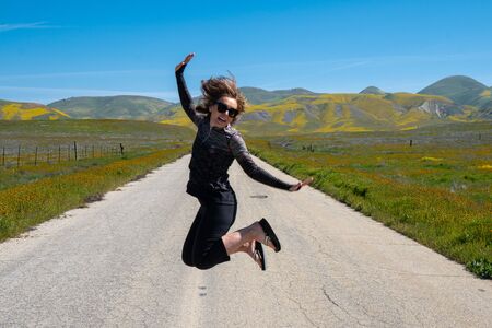 Woman jumping in the middle of the empty road in Carrizo Plain National Monument during the California superbloomの写真素材