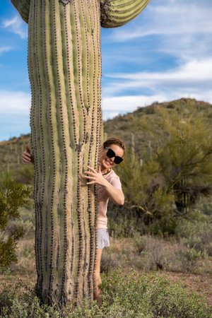 Cute female woman stands next to a large Saguaro cactus in the Sonoran desert, giving it a hug with her armsの写真素材