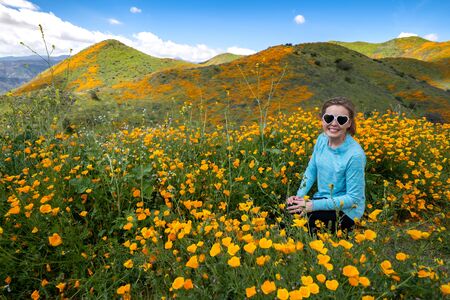 Young woman wearing heart sunglasses and casual clothing poses in poppy fieldの写真素材