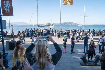JULY 7 2017 - SAN FRANCISCO, CALIFORNIA: Tourist woman takes photos of Alcatraz from Pier 39 at a busy area of the pier, with crowds of touristsのeditorial素材