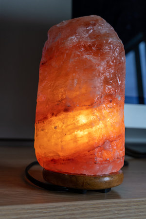 An orange pink glowing himalayan salt lamp sits on a computer desk. Calming concept at work