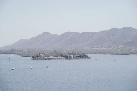 View of Lake Pichola and floating palace, mountains in the background in Udaipur, Indiaの写真素材