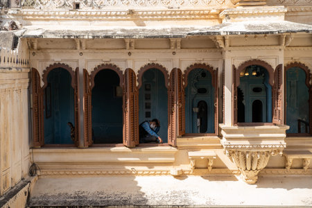 Udaipur, Rajasthan India - March 14, 2020: Beautiful outdoor intricate walls of the City Palace in Udaipur, as a man wearing a face mask sits in a windowsill during the Coronavirus outbreakのeditorial素材