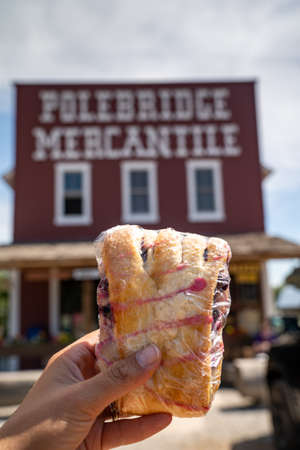 Polebridge, Montana - July 28, 2020: The famous Polebridge Mercantile, a bakery and shop in the small community in Glacier National Park. Hand holds up a famous huckleberry bear clawのeditorial素材