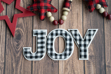 Black and white joy plaid phrase on a wood background with red stars, useful for Christmas projects