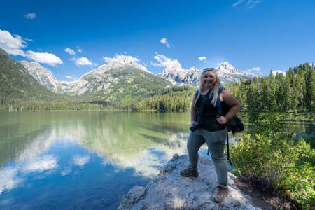 Proud blonde woman hiker stands on a rock on the shoreline of Taggart Lake, in Grand Teton National Parkの写真素材