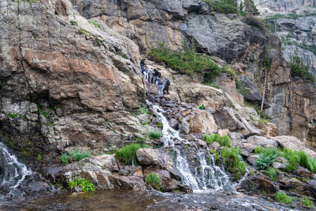 Colorado, USA - August 1, 2021: Hikers scramble up the slippery waterfall along the Sky Pond trail...