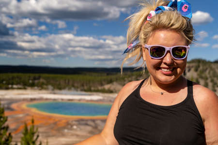 Cute, stylish blonde woman poses at the Grand Prismatic Spring overlook in Yellowstone National Parkの写真素材