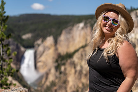 Happy tourist young woman poses wearing a hat at the Grand Canyon of the Yellowstone Artists Point overlook with waterfallの写真素材