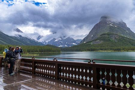 Montana, USA - July 4, 2022: Tourists on the deck of the Many Glacier hotel use binoculars to spot wildlife in Glacier National Parkのeditorial素材