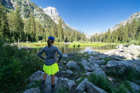 Woman has hands on hips as she enjoys and views the scenery at a pond along the Cascade Canyon Trail in Grand Teton National Parkの写真素材