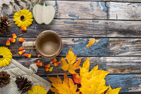 Cozy autumn fall arrangement flatlay with coffee, candy corn, maple leaves, pine cones on a blue...