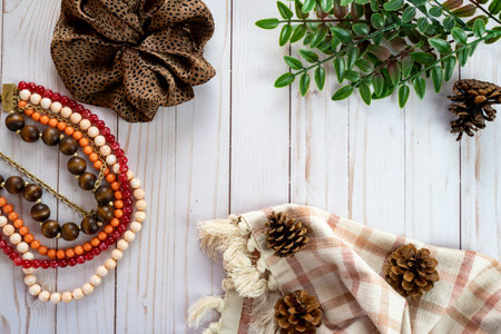 Trendy flat lay top down view with a brown scrunchie, pine cones, plaid towel, green leaves, and a...