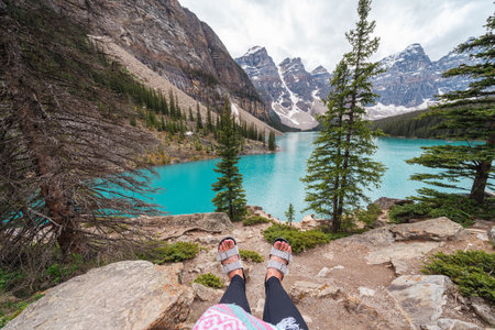 Moraine Lake in Banff National Park on an overcast day, with a woman sitting on the rocks, only feet in sandals showingの写真素材