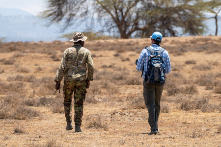Lake Naivasha, Kenya - March 4, 2023: Armed guard and a man tourist on a walking safari on Crescent Island look for wildlifeのeditorial素材