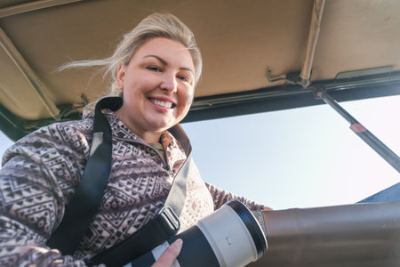 Woman wildlife photographer smiles with the pop up top of a safari vehicle looking for animals in Kenya Africaの写真素材