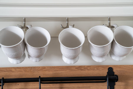 White porcelin coffee cups, hanging in a kitchen storage shelfの写真素材