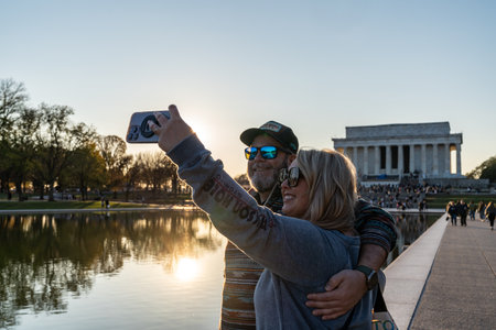 Washington, DC - November 12, 2023: Man and woman take a selfie at the reflecting pool near the Lincoln Memorial at sunsetのeditorial素材