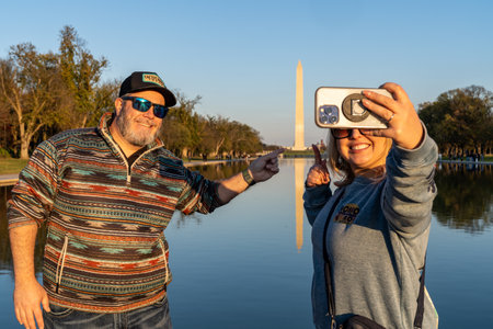 Washington, DC - November 12, 2023: Man and woman take a selfie at the reflecting pool pointing to the Washington Monument at sunsetのeditorial素材