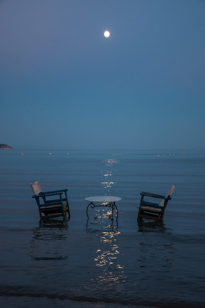 Table and two chairs in the sea for romantic dinner in moonlightの写真素材