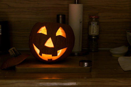 Freshly hollow pumpkin as jack-o-lantern glowing in the dark on the kitchen tableの写真素材
