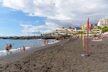 Puerto de Santiago, Tenerife, Spain - September 20, 2022: People sunbathing on famous volcanic beach. The beach is one of the cleanest on the island, and has been awarded the European Blue Flagのeditorial素材