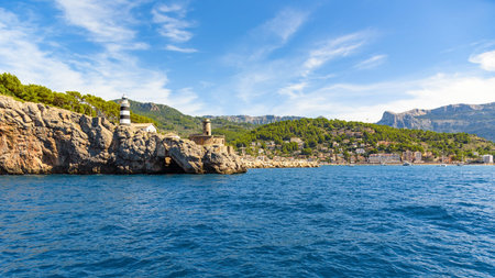 Beautiful coastal scene showing the black and white lighthouse of Port de Soller, rugged cliffs, and the calm blue waters of the Mediterranean sea in Mallorca, Spainの写真素材