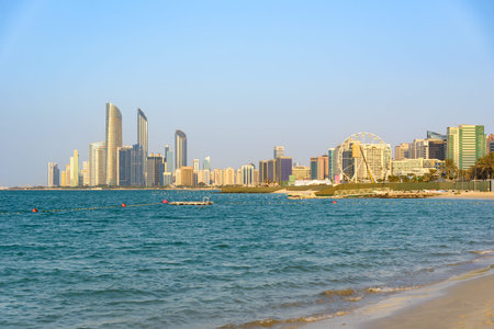 Scenic landscape capturing the modern skyscrapers of the Abu Dhabi Corniche glowing in the warm golden light of the late afternoon sun, viewed across the calm waters of the Arabian Gulfの写真素材