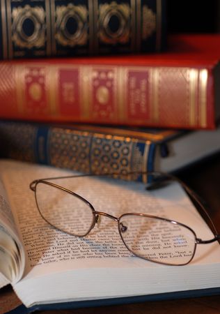 A pair of reading glasses on a book with a stack of old books in the backgroundの写真素材