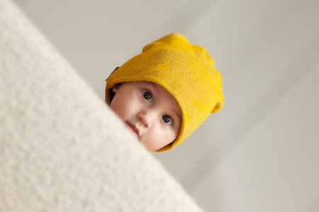 Cute Baby with a Beanie Hat behind a Sofa